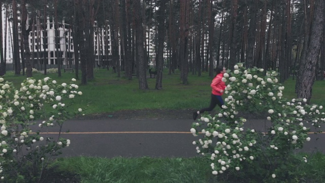 下雨天独自在公园慢跑的女人。身着橘色夹克的黑发女子在城市公园的人行道上奔跑。女运动员在户外新鲜空气下训练。运动理念，健康生活方式视频下载