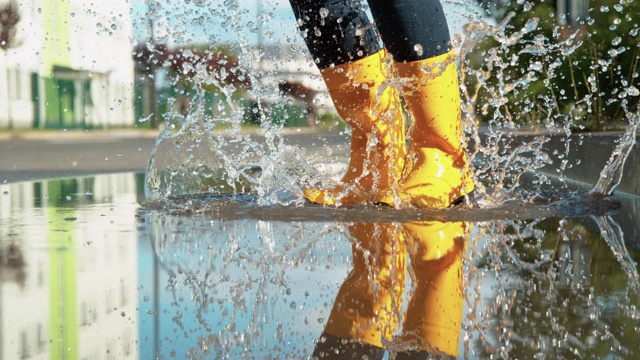 特写:无忧无虑的年轻女子在黄色雨靴跳进大水坑。视频下载