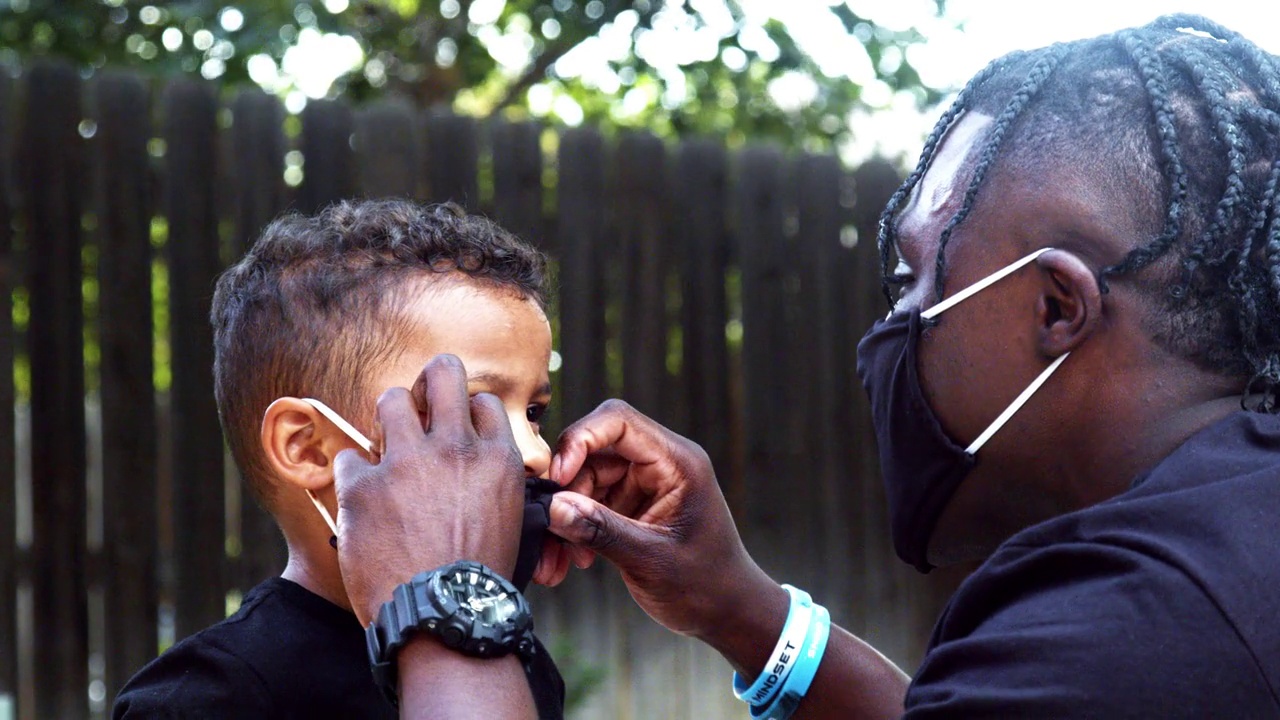 一名非洲裔美国父亲正在帮助他三岁的混血儿子戴上个人防护口罩，以抵御新冠肺炎疫情的蔓延视频下载