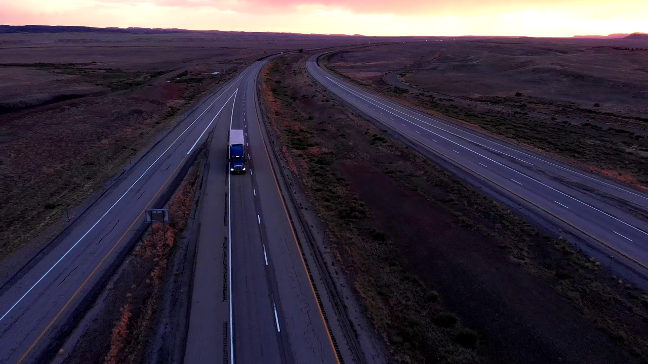在黄昏或黎明时分，在荒凉的沙漠中，在一条四车道的公路上行驶视频下载