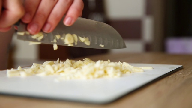女孩用刀在木板上切大蒜。厨房里的女人切碎剥皮的大蒜视频下载
