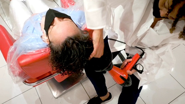 女蒙面发型师在美容院重开时吹干顾客的头发视频下载