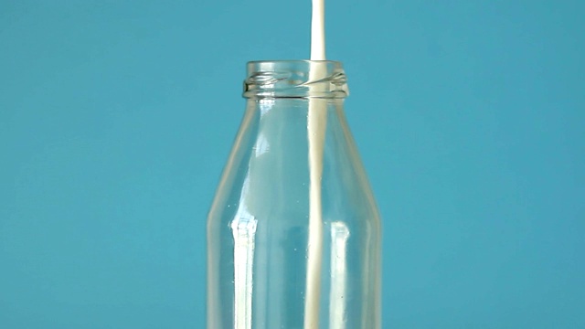 新鲜的农场牛奶是倒进玻璃瓶在蓝色背景前视图。近距离视频下载