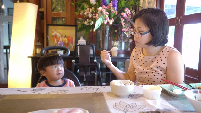在一家日本餐馆里，亚洲母亲在给儿子喂食前检查食物温度。视频下载