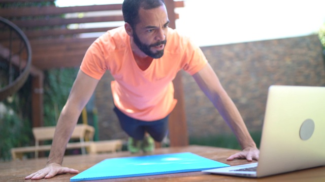 一个在家上虚拟健身课的男人在做俯卧撑视频素材