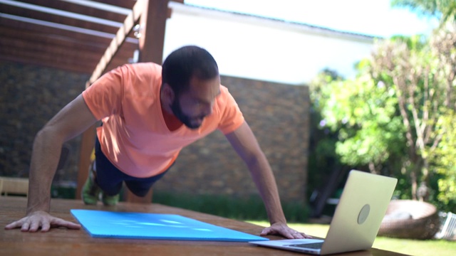 一个在家上虚拟健身课的男人在做俯卧撑视频素材