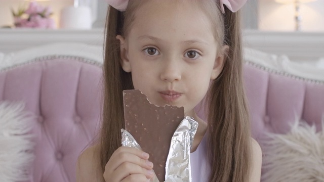 小女孩在家里吃巧克力的特写。满意的面孔漂亮的黑发白种人孩子与棕色眼睛享受不健康的甜食室内。快乐的孩子吃甜点视频素材