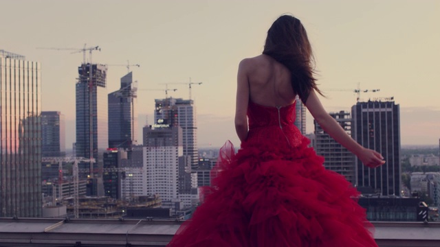 在屋顶上跳舞的解放女性。穿着红色的礼服欣赏城市全景视频下载