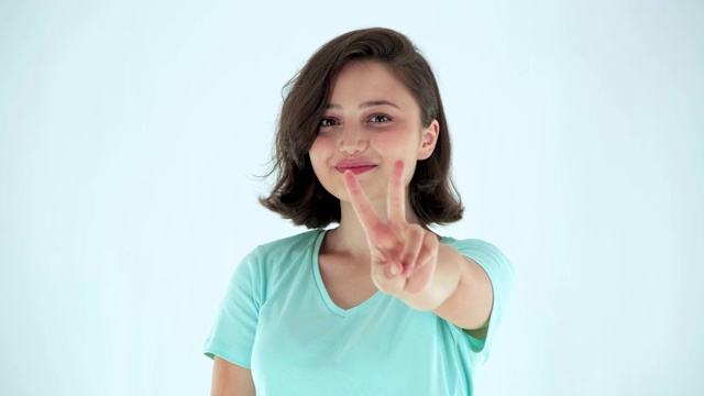 在白色背景上显示胜利或和平标志的年轻女子。快乐的女孩伸出两根手指。视频素材