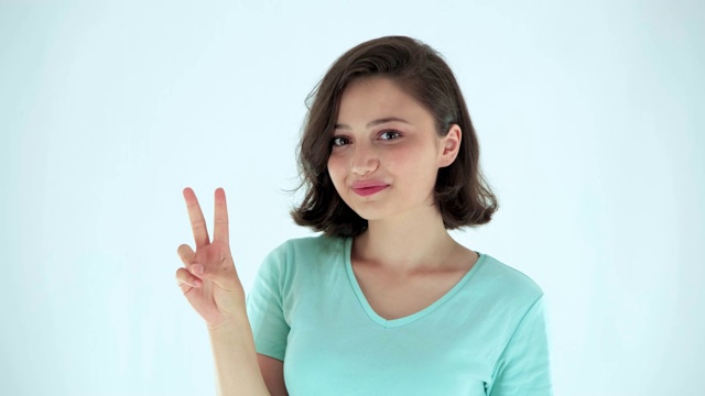 在白色背景上显示胜利或和平标志的年轻女子。快乐的女孩伸出两根手指。视频素材