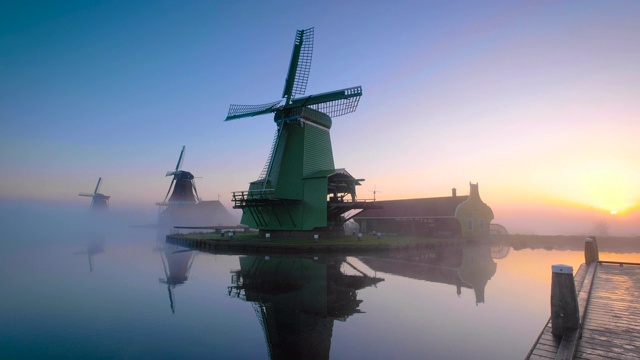 荷兰传统的风车在日出时的薄雾中沿着Zaanse Schans运河在荷兰视频下载