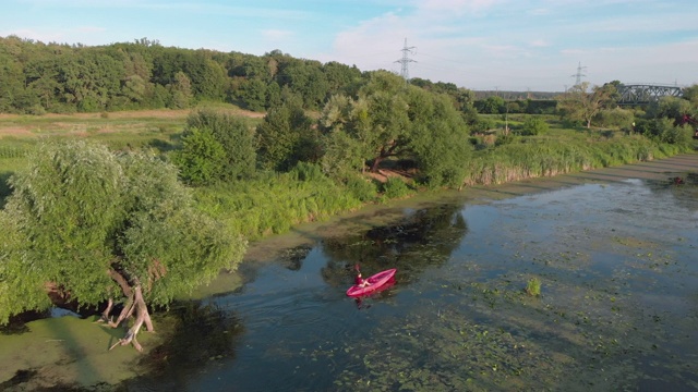 无人机俯视图的妇女在河上漂浮在船上在阳光明媚的夏日。女游客正在湖上划皮艇。夏天，女孩乘着独木舟探索美丽的乡村风景。水旅游。运动划船视频下载
