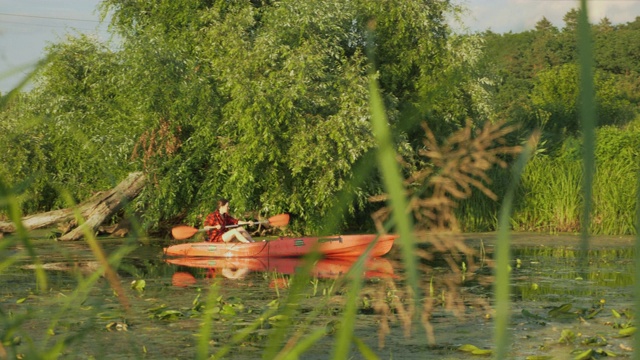 爱玩的女人在平静的河上划船。夏天，一名女游客在湖中划着独木舟。健身女孩在假日的周末乘皮划艇沿河漂流。旅行者在水上划皮艇视频下载