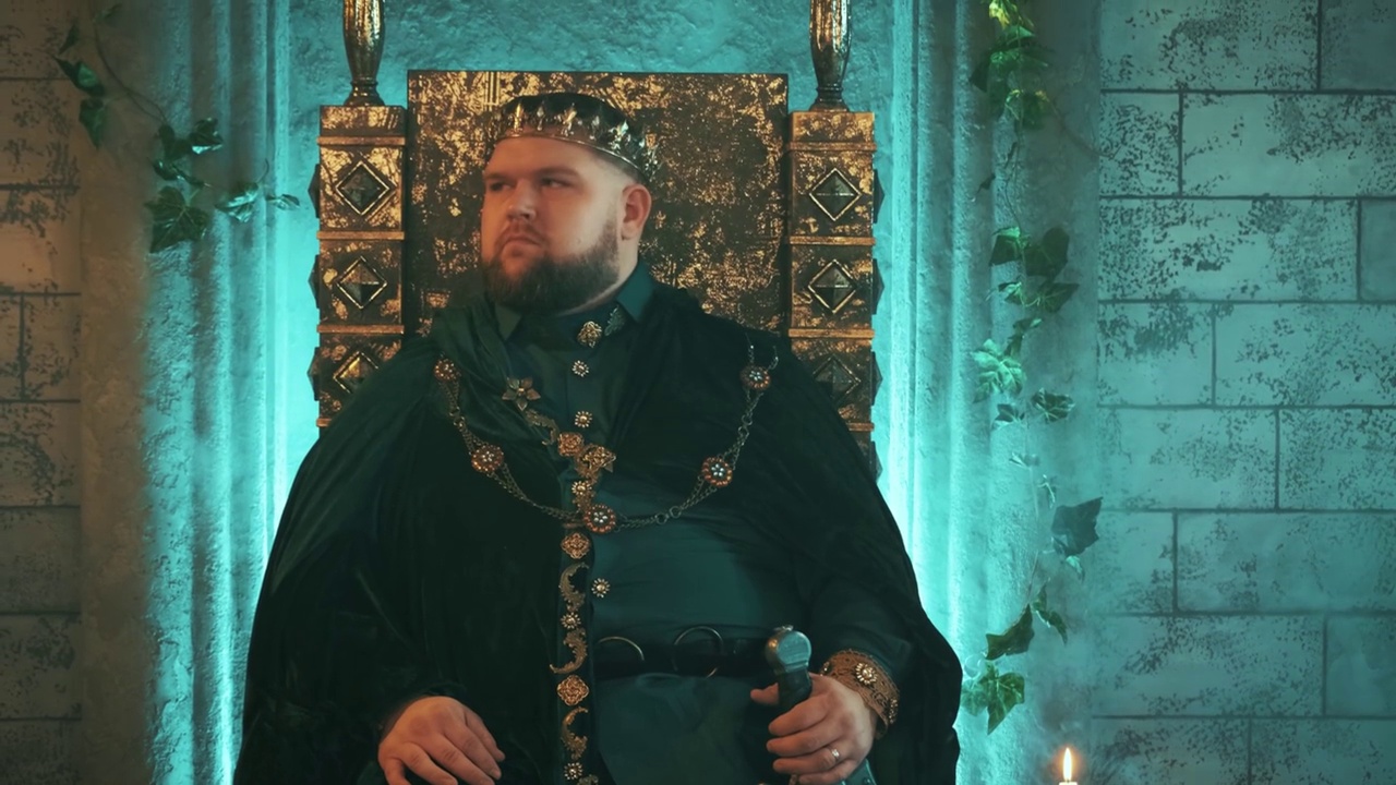 中世纪的壮汉国王坐在古老的青铜宝座上，手持剑和金王冠视频下载