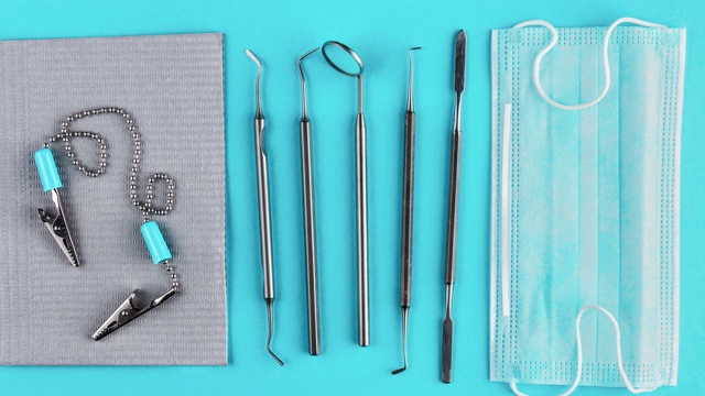 一套金属牙医工具，灰色防水餐巾，医用口罩隔离在蓝色背景上。钢制口腔镜，牙周探伤器，镊子等工具。牙齿保健的概念视频素材