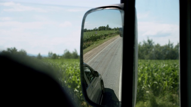 卡车司机窗户和镜子的视图。在温暖的夏日，一个男人在乡间路上开车。慢镜头视频下载