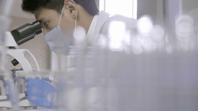 在实验室里通过显微镜进行研究的亚洲科学家。视频素材