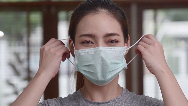 一名穿着休闲服装的亚洲女子正摘下面具，对着镜头微笑。传达新冠肺炎疫情好转的信息。视频素材
