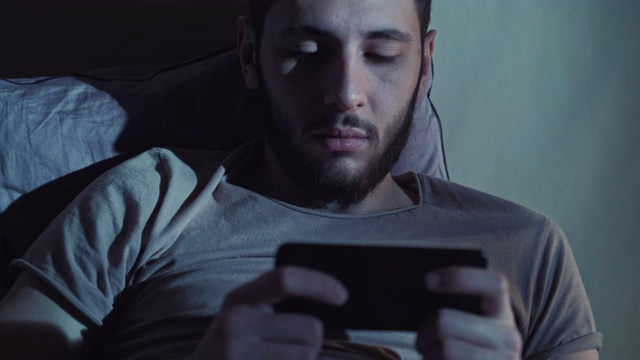 夜不成寐的男人在电话床上玩网络游戏视频素材