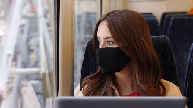 用手提电脑戴口罩，乘火车旅行。视频素材