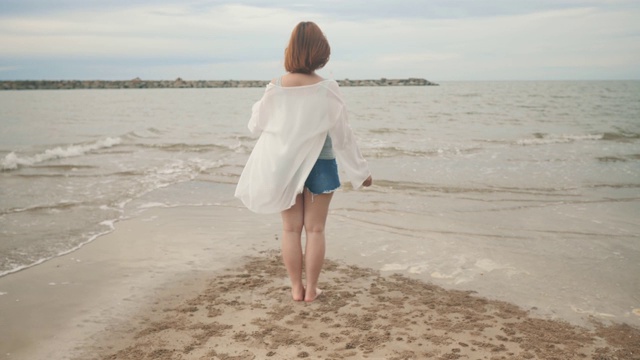 快乐女人光着脚站在沙滩上，双手高举，4K视频素材