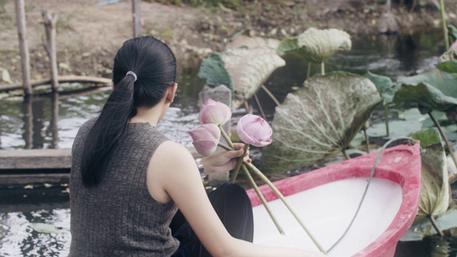 一名亚洲女子在荷塘里划着小船，采荷花，折荷花。在自然环境中放松的概念。视频素材