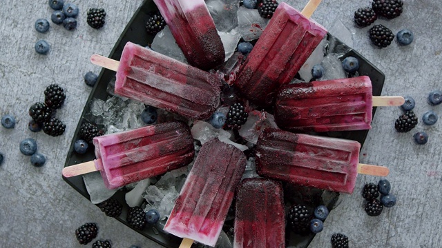 自制的新鲜蓝莓和黑莓冰棒放在黑色的盘子上，冰放在石头上视频素材