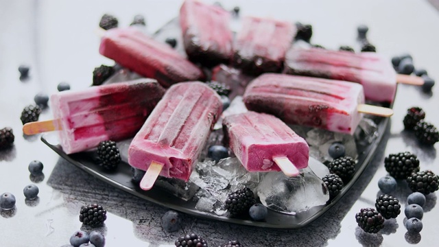 自制的新鲜蓝莓和黑莓冰棒放在黑色的盘子上，冰放在石头上视频素材