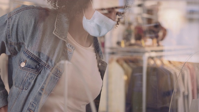 2019冠状病毒病大流行期间，佩戴防护口罩的顾客在服装店用智能手机支付视频素材