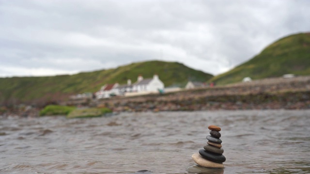 英国海边的Saltburn海边的卵石塔，以模糊的酒吧和山为背景的河里的禅意石堆砌，海滩上的堆砌石金字塔象征着稳定、和谐、平衡，景深浅。视频素材