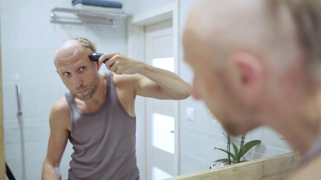 4K男人在浴室镜子前用电动剃须刀把头发剃光视频下载