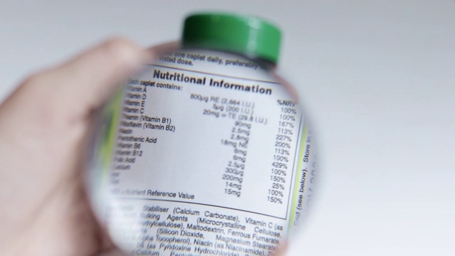 特写检查营养信息标签上的一瓶补充剂与放大镜视频下载