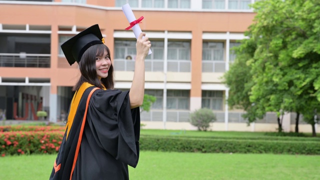 亚洲女毕业生身穿黑色长袍，头戴金色流苏的黑色帽子。拿着文凭微笑着祝贺大学视频素材