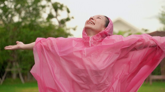 一位美丽的亚洲妇女穿着雨衣在雨中玩耍。她高兴地笑了。视频下载