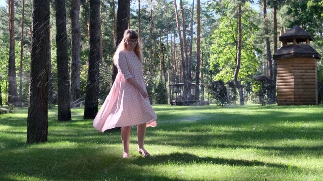 灌溉期间，年轻女子在草坪上纺纱。阳光下穿着浅粉色衣服的金发女孩视频下载