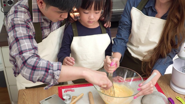 高角度视图:一个十几岁的女儿和父亲看着母亲用手搅拌准备面粉。亚洲家庭的概念，一个孩子做饭，烘焙。十几岁的女孩有积极的情绪和兴奋去做这件事。视频素材