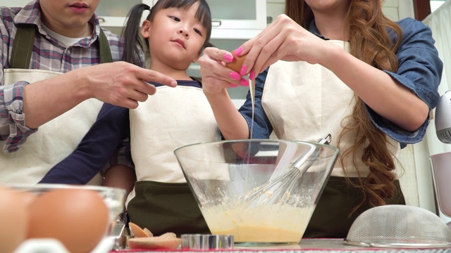 低视角:一个十几岁的女儿，父亲和母亲在周末一起敲鸡蛋做面包准备。亚洲家庭的概念，一个孩子做饭，烘焙。十几岁的女孩有积极的情绪，微笑，兴奋地去做。视频素材