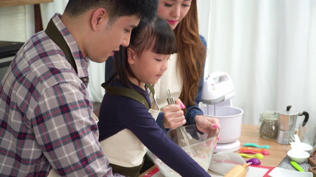 侧面图:十几岁的女儿、父亲和母亲用手搅拌准备面粉。亚洲家庭的概念，一个孩子做饭，烘焙。十几岁的女孩有积极的情绪和兴奋去做这件事。视频素材
