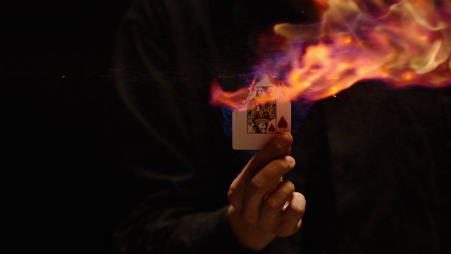 一个魔术师的手表演皇后卡戏法的特写。燃烧卡在黑色背景和烟雾。手握燃烧牌的卡片机械师。拍摄在ARRI Alexa电影摄影机在慢动作视频下载