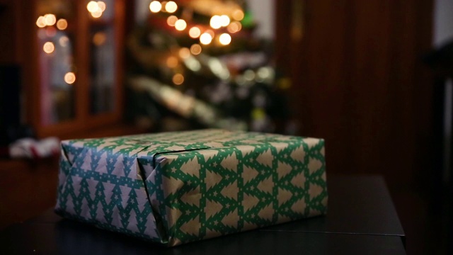 手的特写，把最后一层胶布粘在包装纸上，包装纸上包裹着客厅里的礼物，后面是圣诞树上的散焦灯视频下载