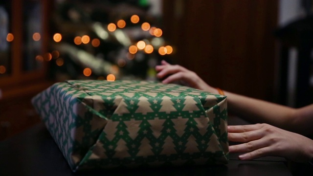 在家里的客厅里，手在礼物盒上安排包装纸，后面是圣诞树灯的散焦视频下载