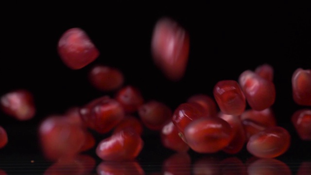 松脆的种子。超级慢镜头的石榴种子下落和滚动在黑色的背景。石榴颗粒接近4K视频。健康饮食，水果理念。视频下载