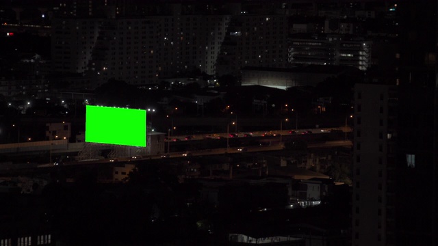 4K鸟瞰图绿色屏幕或色度键广告显示监控广告牌在城市街道上繁忙的交通驾驶汽车的道路和高速公路上照亮市中心地区的夜晚灯。视频下载