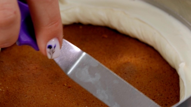 厨师用金属铲将奶油涂在蛋糕上的特写。视频素材
