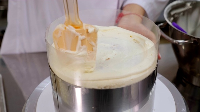 厨师用金属铲将奶油涂在蛋糕上的特写。视频素材