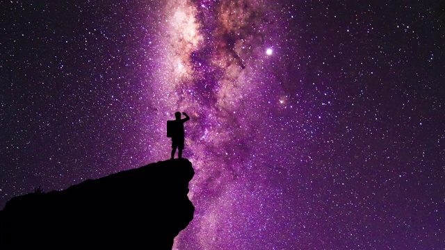 一个背包客的剪影站在悬崖边凝视着银河和流星视频下载