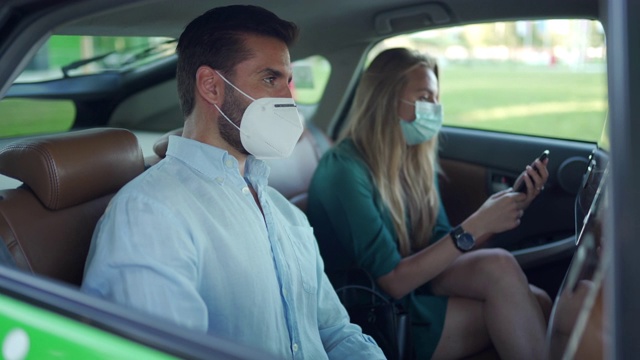 一名男子和一名女子戴着防护口罩，坐在出租车后座用杀菌剂消毒双手视频素材