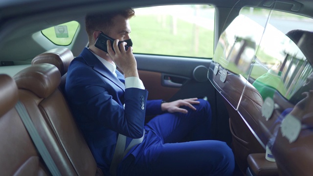 红发商人，戴着防护面罩，坐在出租车后座上使用智能手机视频素材