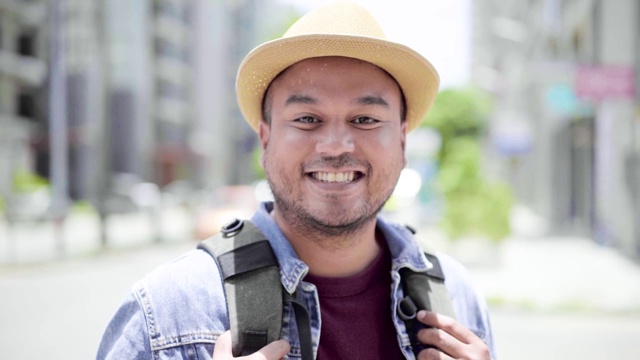 年轻的亚洲背包客在城市中旅行，他微笑着，在街道上竖起大拇指，远离病毒。慢动作镜头。视频下载