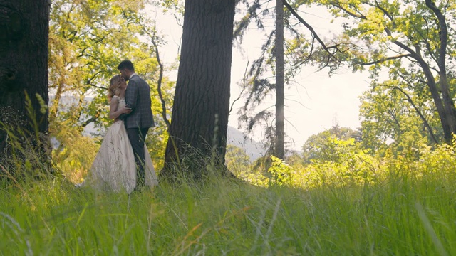 一对年轻的夫妇在树林里相遇在阳光的背景下。新婚夫妇轻轻触碰他们的手，看着彼此的眼睛。视频素材